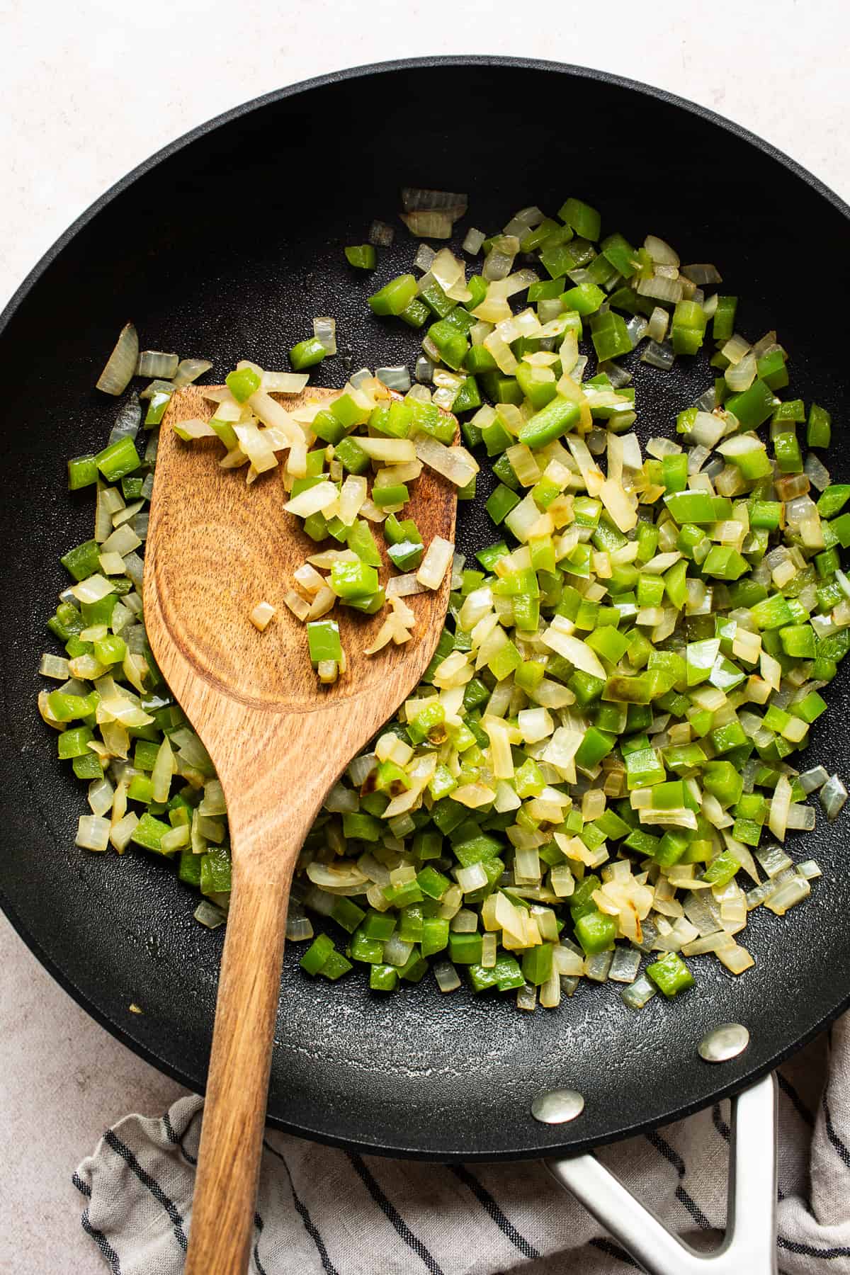 Bell peppers and onions cooking in a skillet with olive oil.