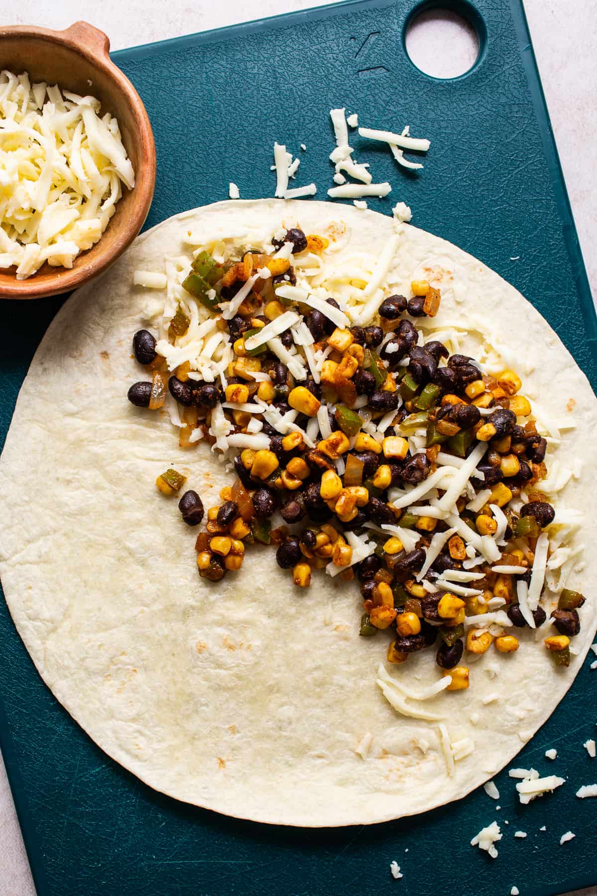 A black bean quesadilla being assembled on a cutting board with shredded cheese.