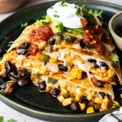 Black bean quesadillas on a plate with sour cream, guacamole and salsa.