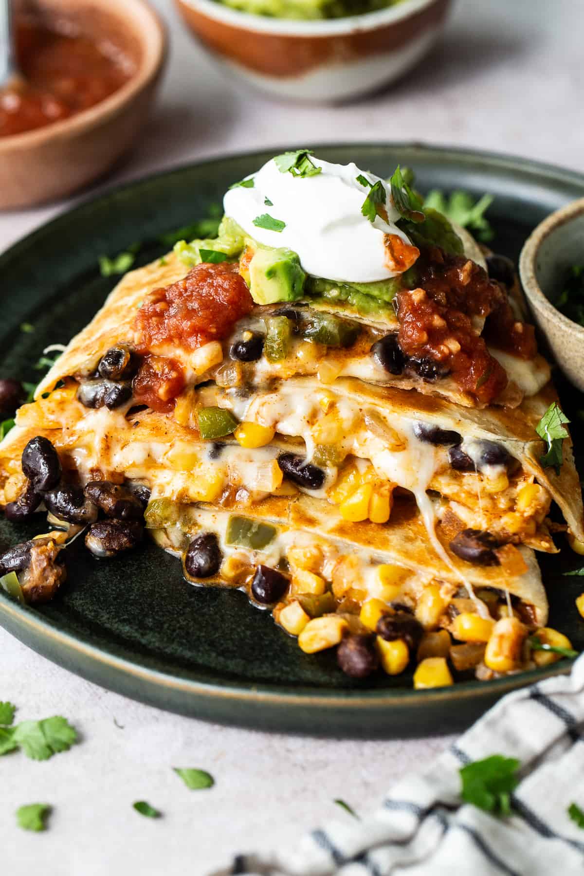 Black bean quesadillas stacked on top of one another served with sour cream, guacamole, and salsa.