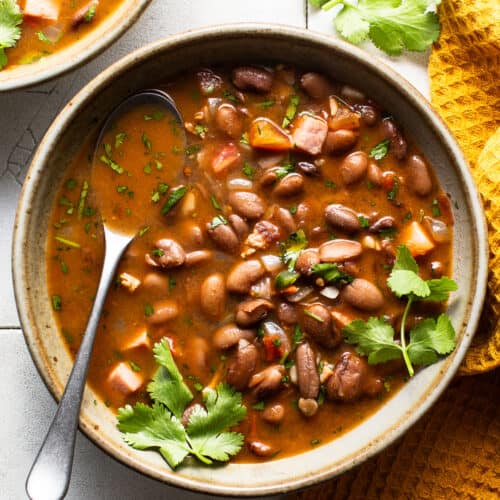 A bowl of charro beans topped with fresh cilantro on a table.