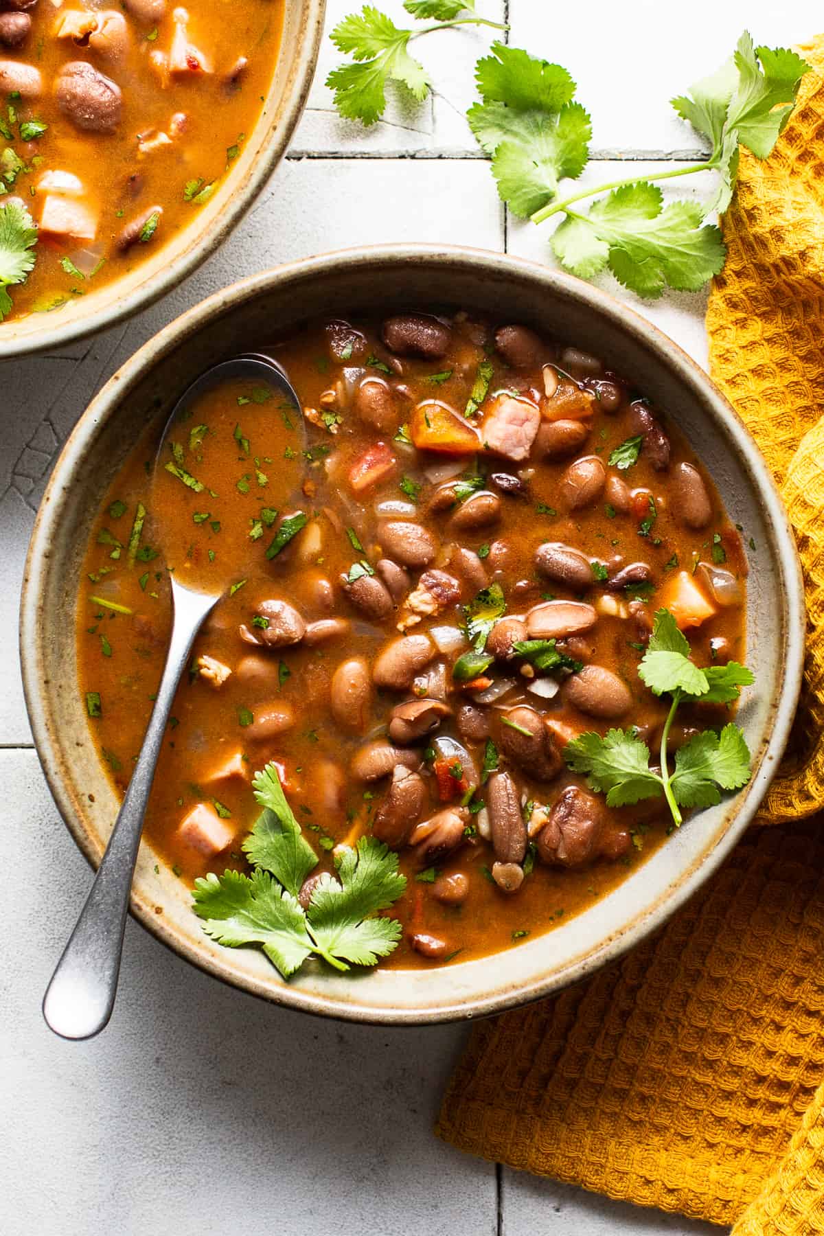 A bowl of charro beans seasoned with fresh cilantro on a table.