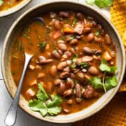 A bowl of charro beans topped with fresh cilantro on a table.