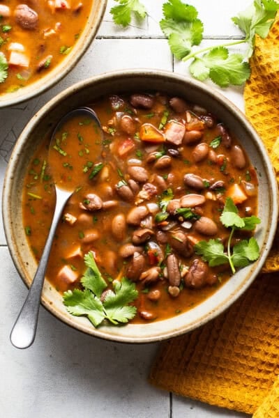 A bowl of charro beans topped with fresh cilantro on a table.