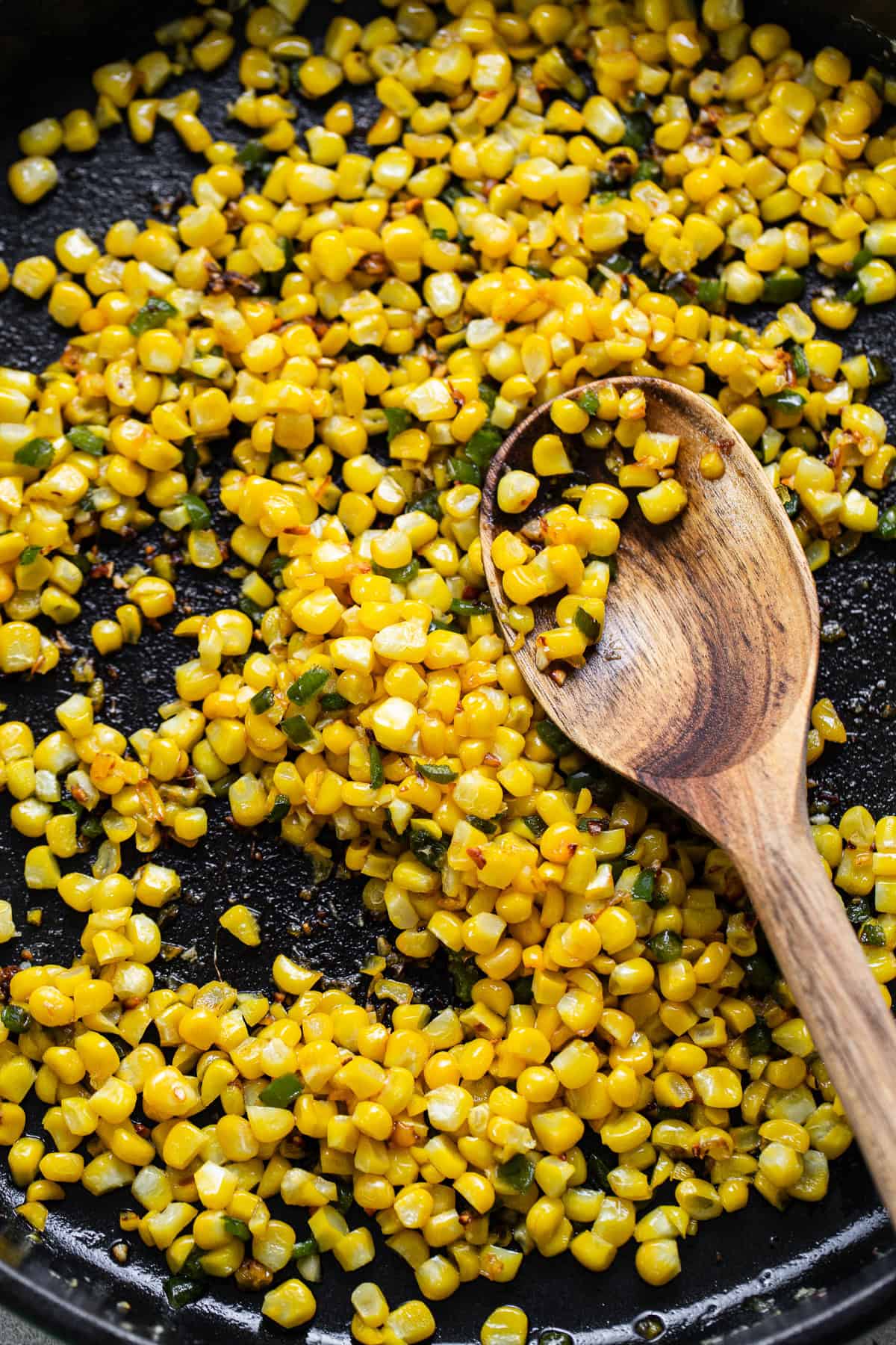 Corn being cooked in a pan with butter, garlic, and jalapenos