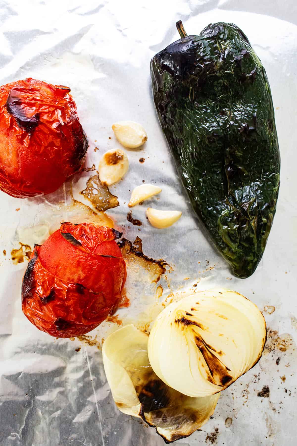 Roasted poblanos, tomatoes, onions, and garlic on a baking sheet.
