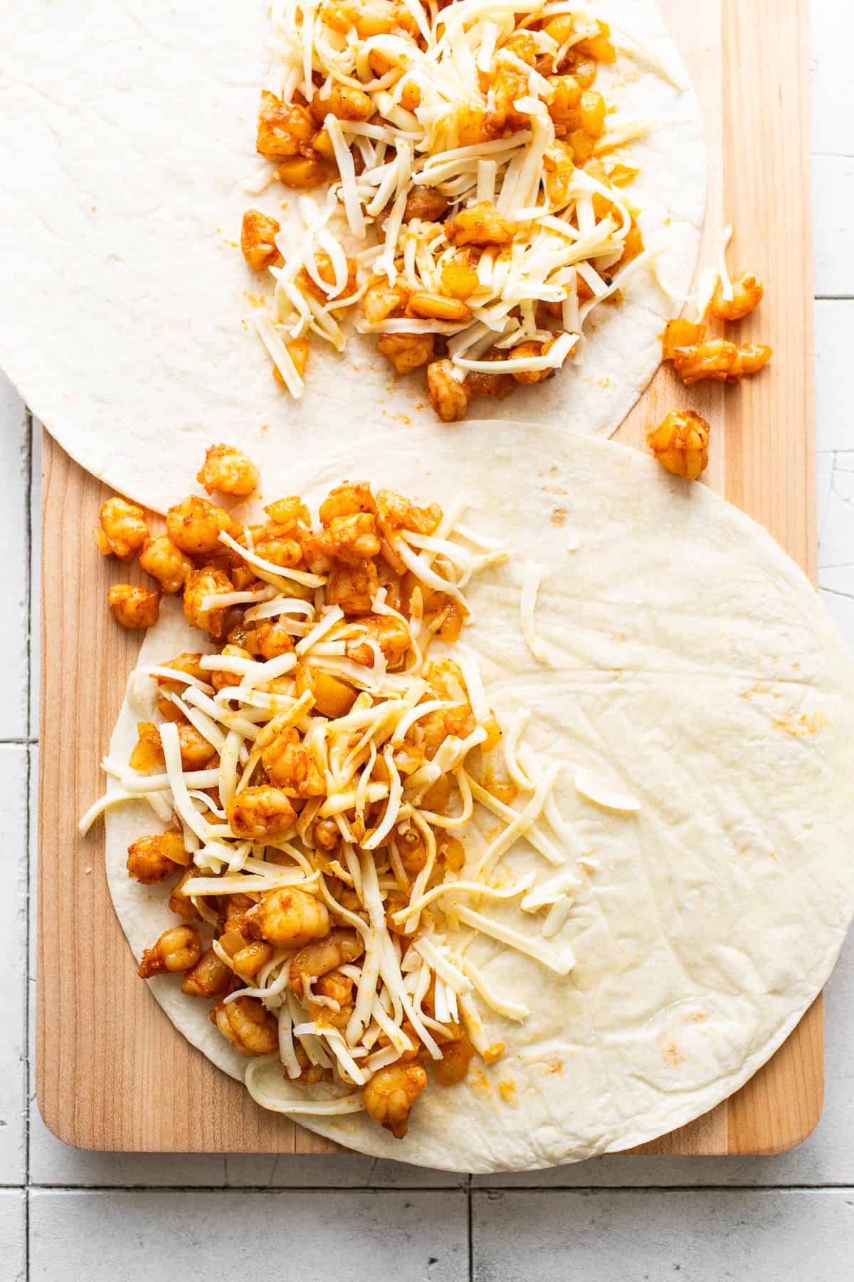 Shrimp and shredded cheese on open flour tortillas for shrimp quesadillas.