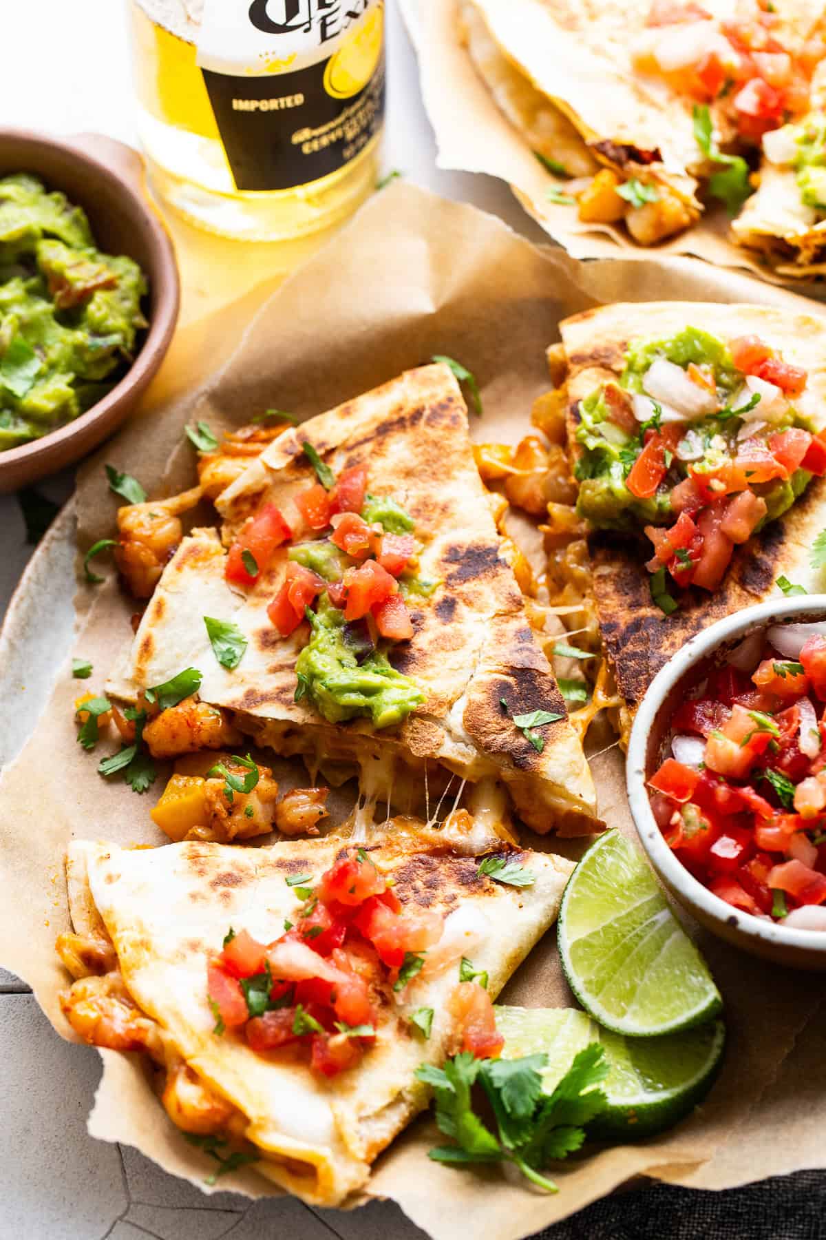 Shrimp quesadillas on a table with pico de gallo and a side of guacamole.