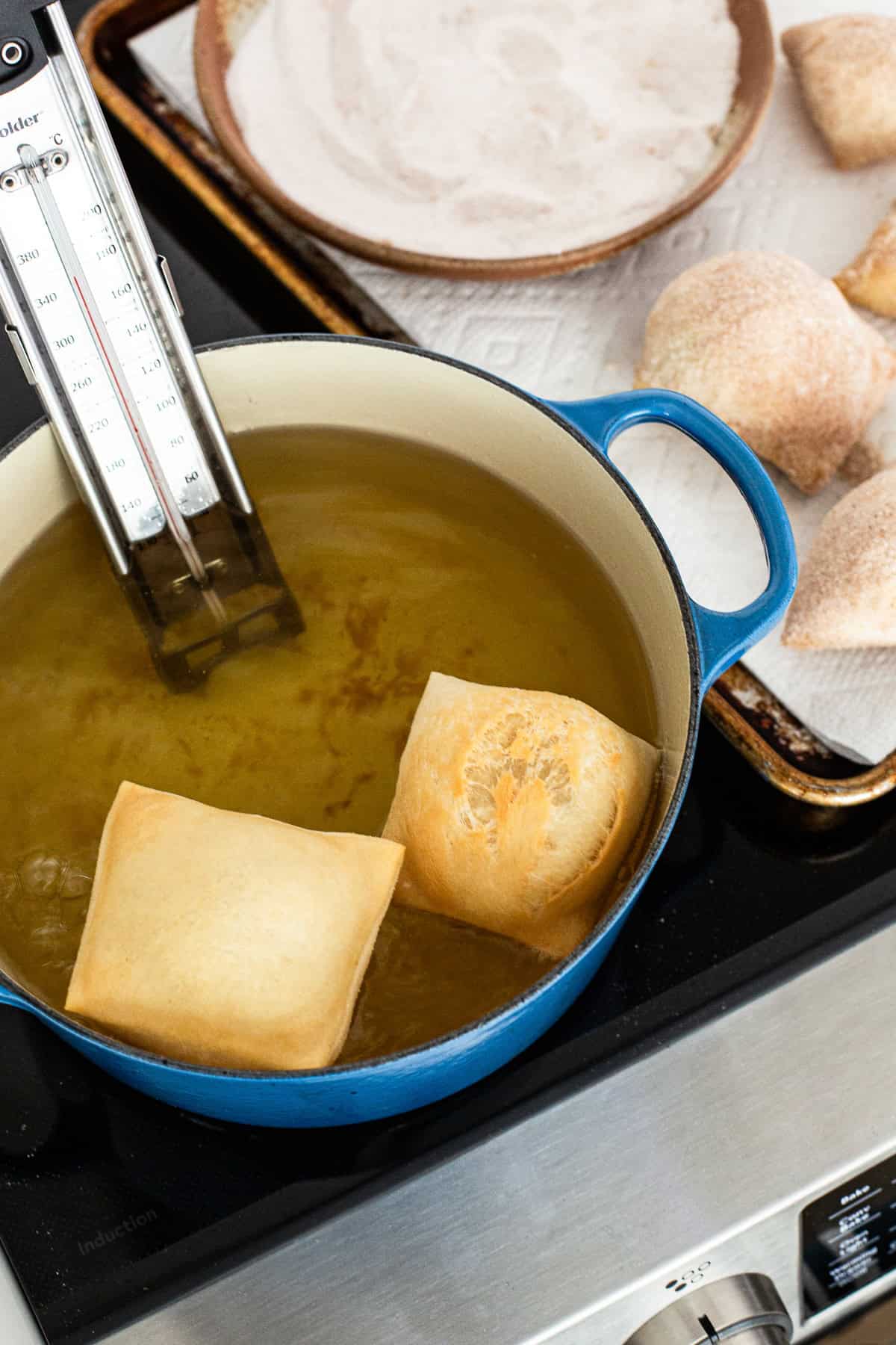 Sopapillas inside a large pot with hot oil to fry them
