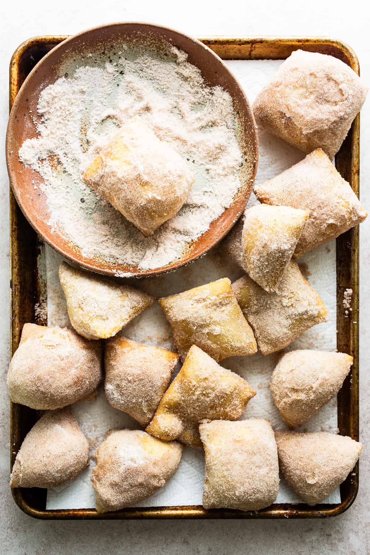 Sopapillas being covered in the cinnamon sugar mixture on all sides