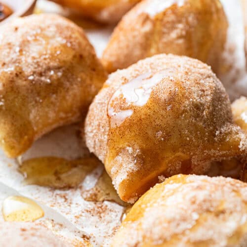 Sopapillas on a plate covered with cinnamon sugar and drizzled with honey.