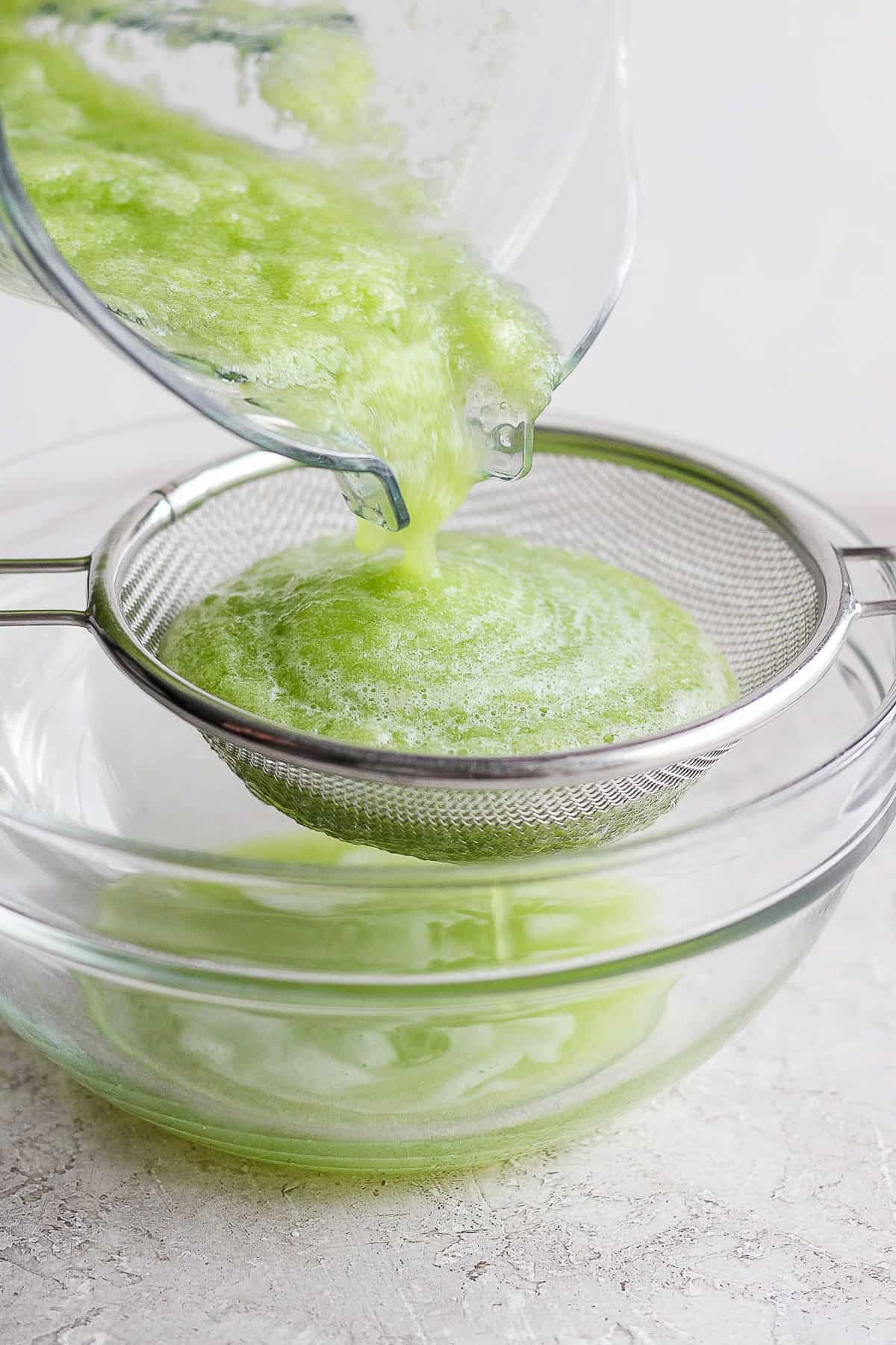 Cucumber juice being strained into a large glass bowl.
