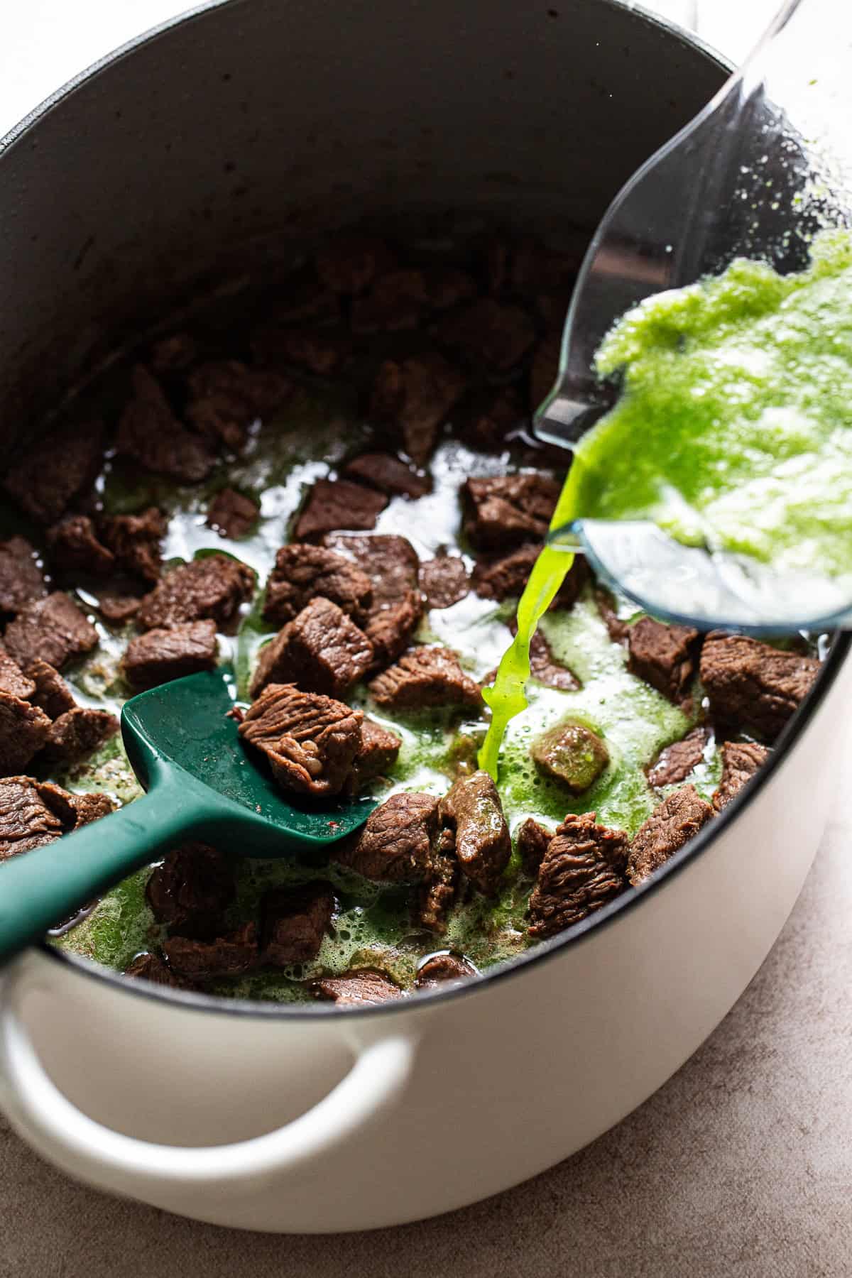 Tomatillo sauce is being poured into the browned beef pot