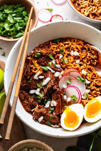 Birra ramen in a bowl topped with cilantro, onion, and radishes and served with a soft boiled egg.