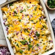 Spinach enchiladas in a baking dish topped with melted cheese, salsa verde, onions, cilantro, and sour cream or Mexican crema.