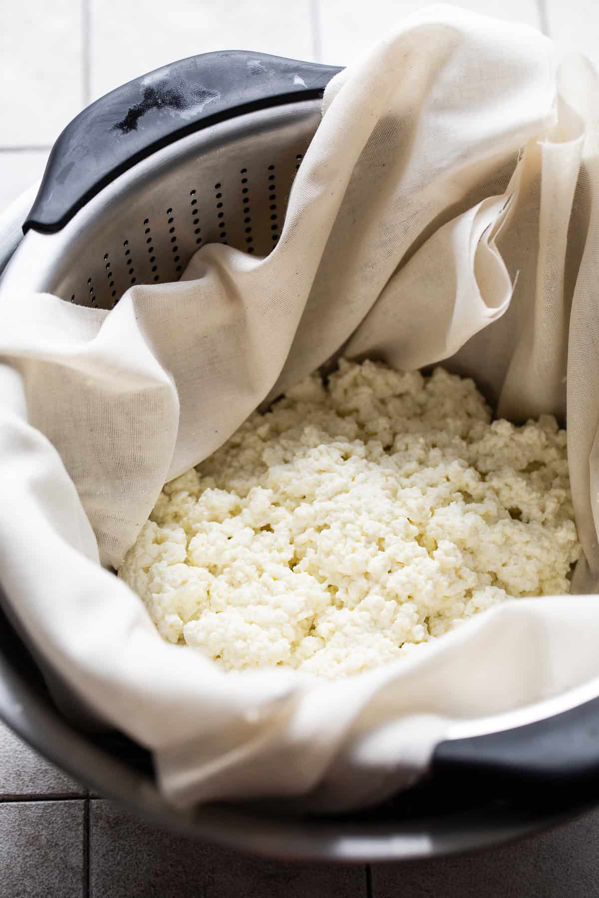 A colander lined with cheesecloth with cheese curds inside.