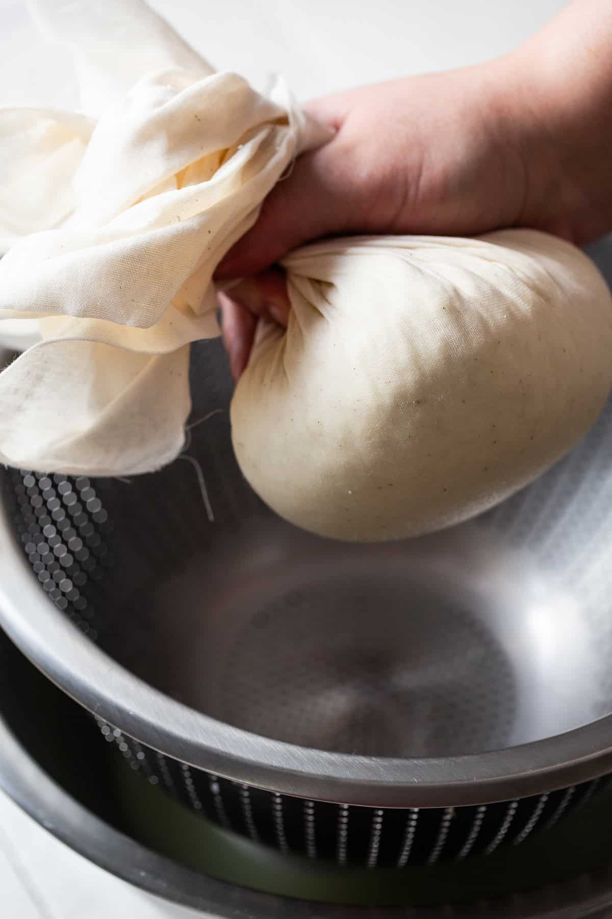 Queso fresco curds being pressed into a ball shape inside the cheesecloth to allow further straining. 