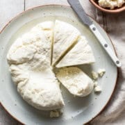 A homemade queso fresco recipe on a plate cut into wedges ready to eat and be sprinkled on Mexican food.