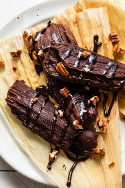 Chocolate tamales drizzled with a chocolate sauce and chopped pecans on a corn husk.