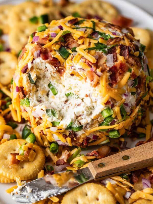 An easy jalapeño cheese ball covered with bacon and cheddar on a plate with crackers.