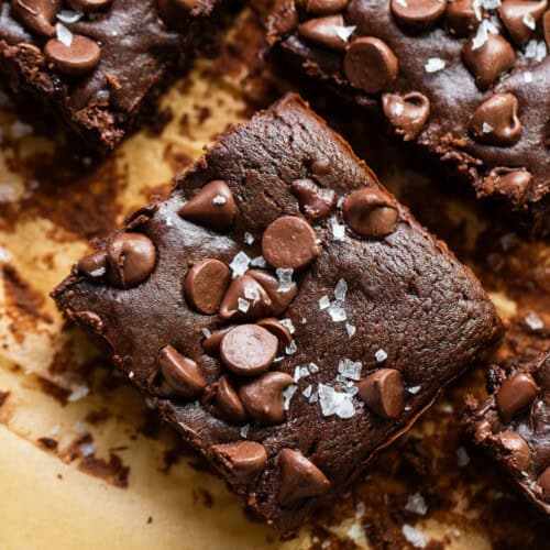 Black bean brownies cut into squares on baking paper covered with flaked sea salt.