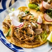 Instant pot chicken tacos served on a dinner plate topped with radishes and limes.