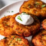Tortitas de papa freshly made and stacked on a dinner plate with a dollop of sour cream.