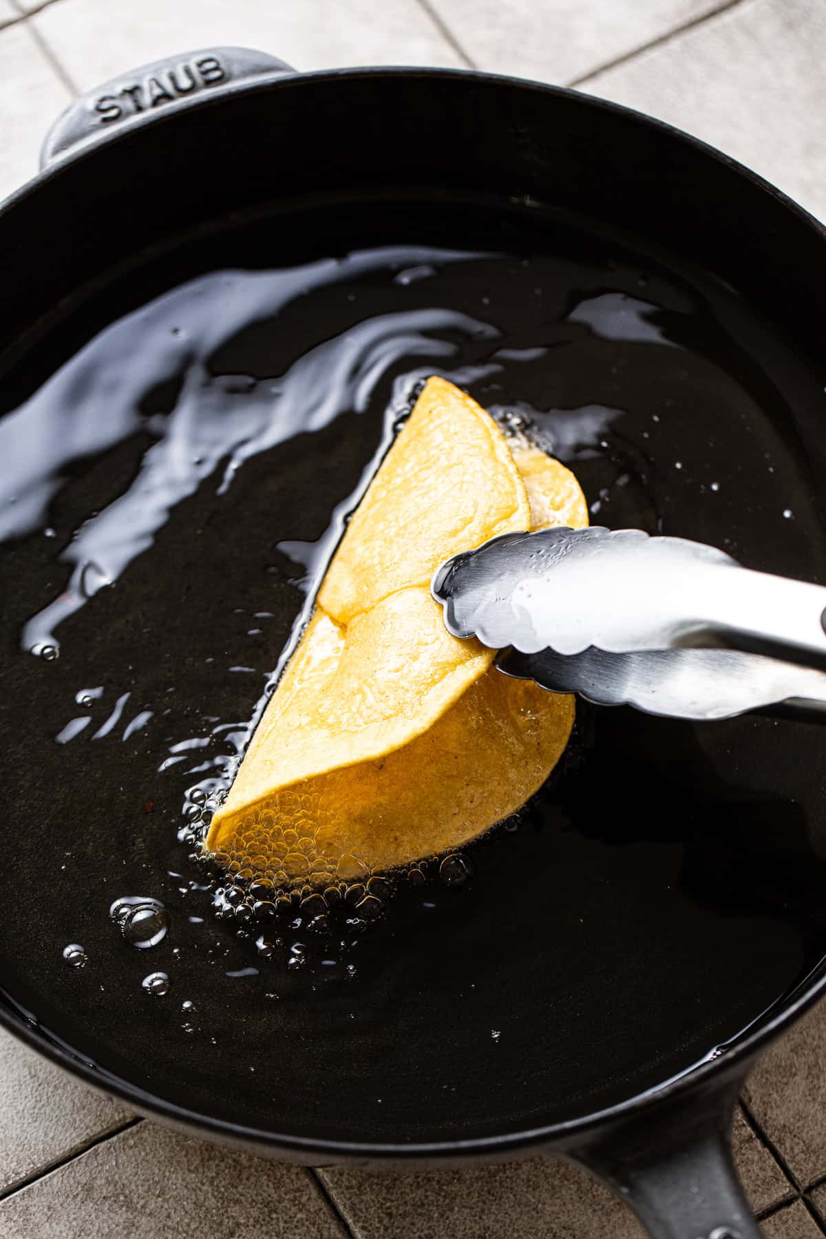 A corn tortilla being fried and shaped into a hard taco crunchy shell.