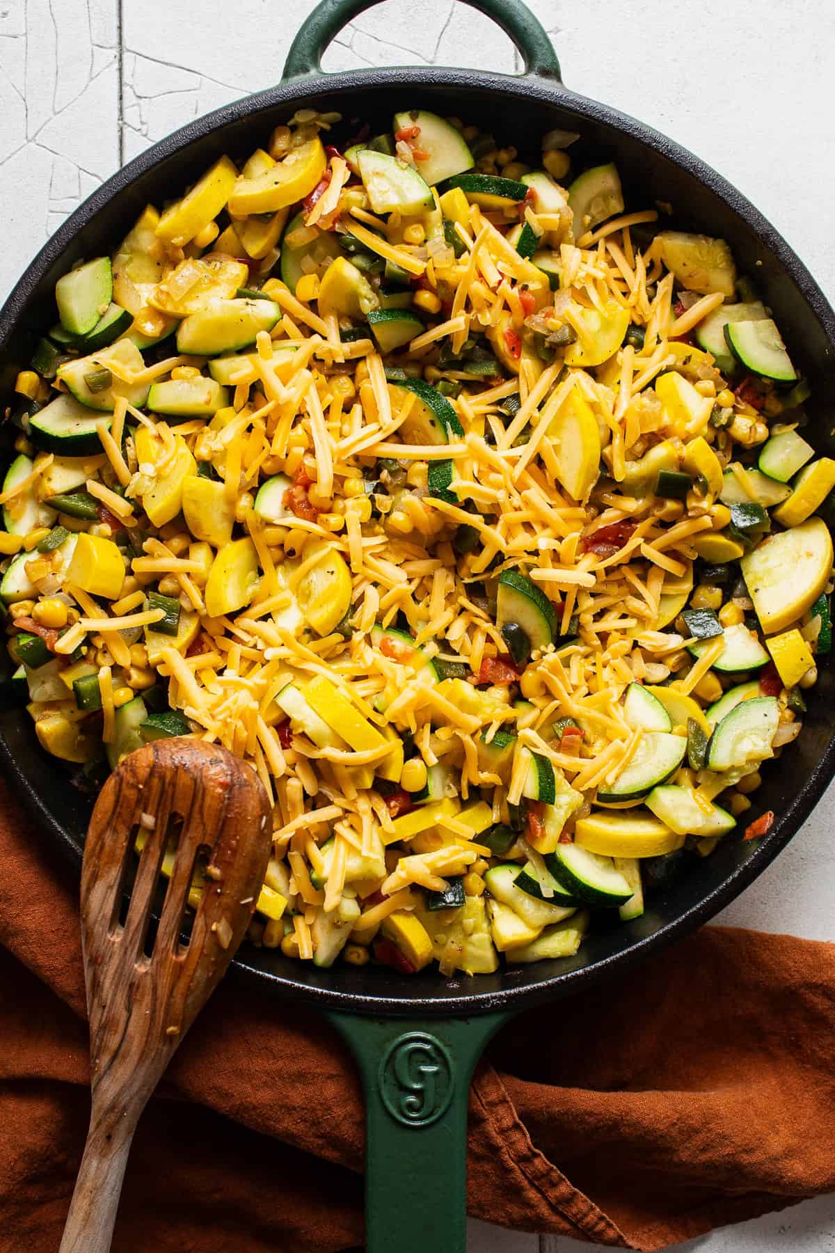 Shredded cheese being mixed into a skillet for a calabacitas recipe.