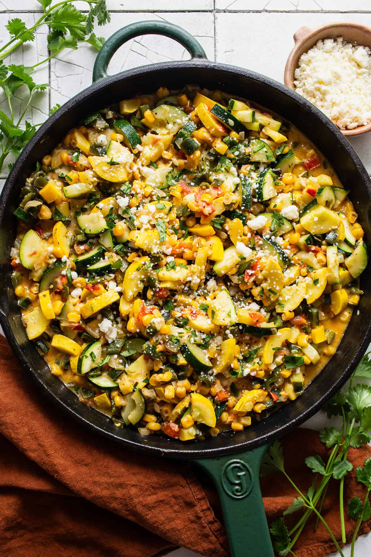 Calabacitas in a skillet topped with cotija cheese and cilantro.