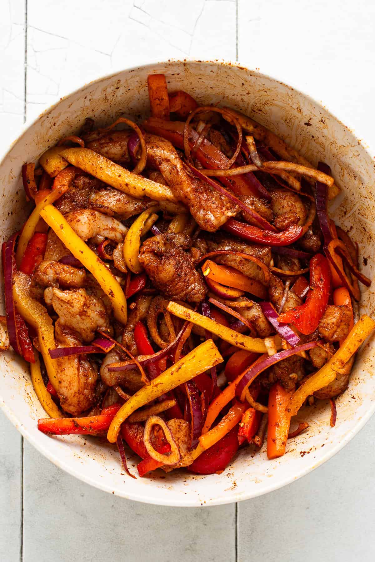A bowl of chicken, bell peppers, and onions seasoned with fajita seasonings.