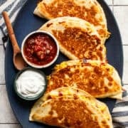 Four crispy and golden breakfast quesadillas on a plate served with salsa and sour cream.