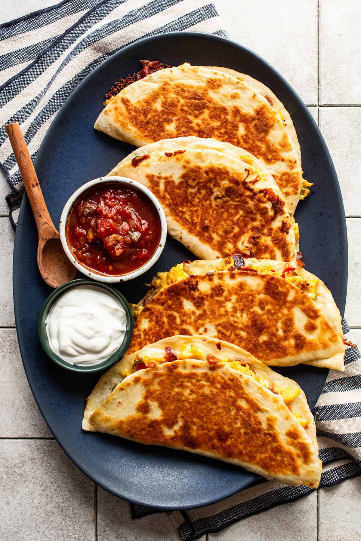 Four crispy and golden breakfast quesadillas on a plate served with salsa and sour cream.