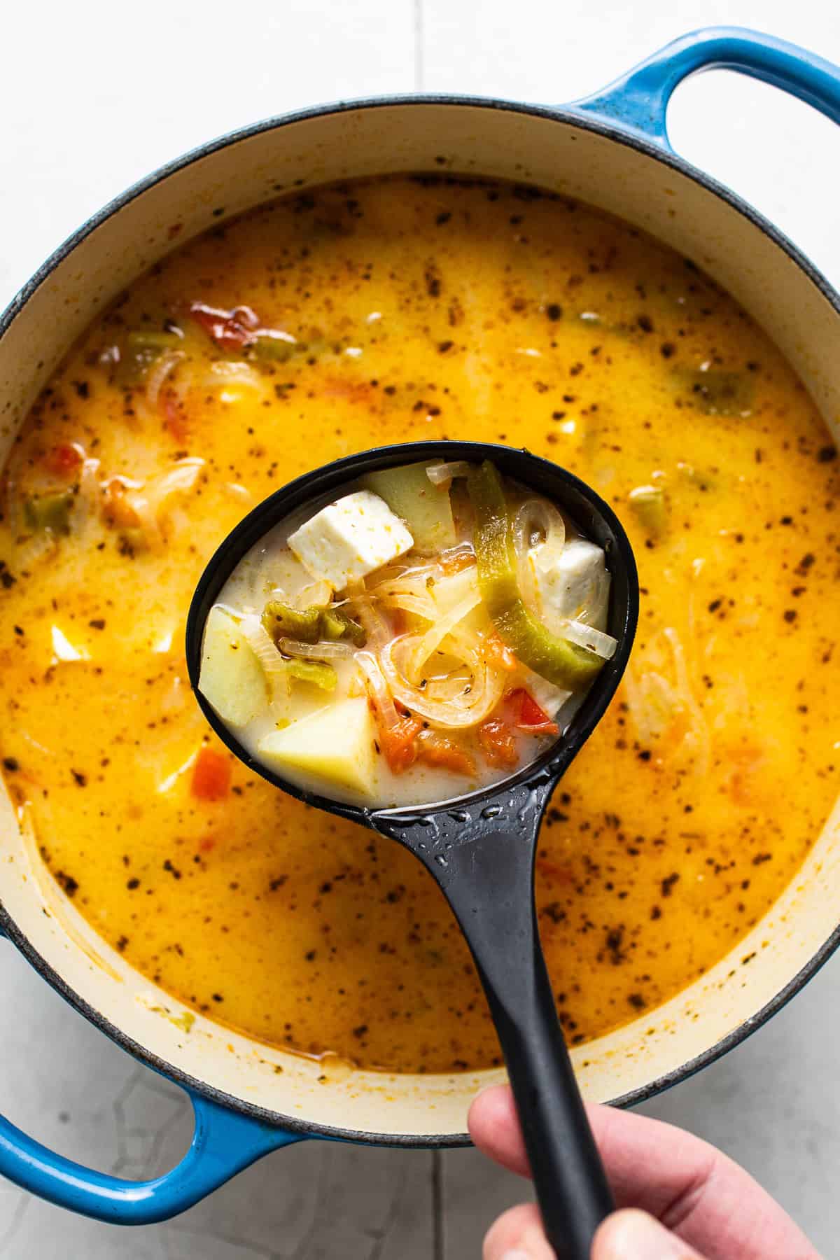 A ladle scooping out a serving of caldo de queso from a pot.