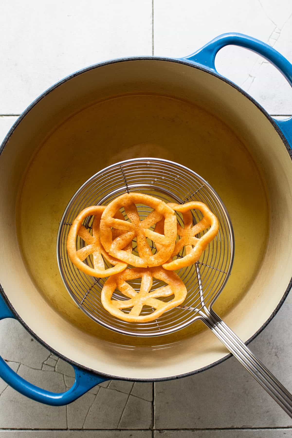 Duros on a spider strainer being shaken off of excess oil.