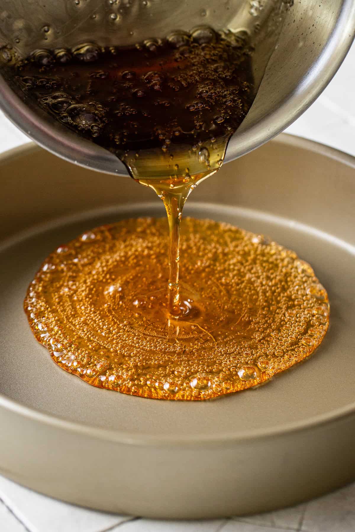 Caramel being poured into a round cake pan for flan.