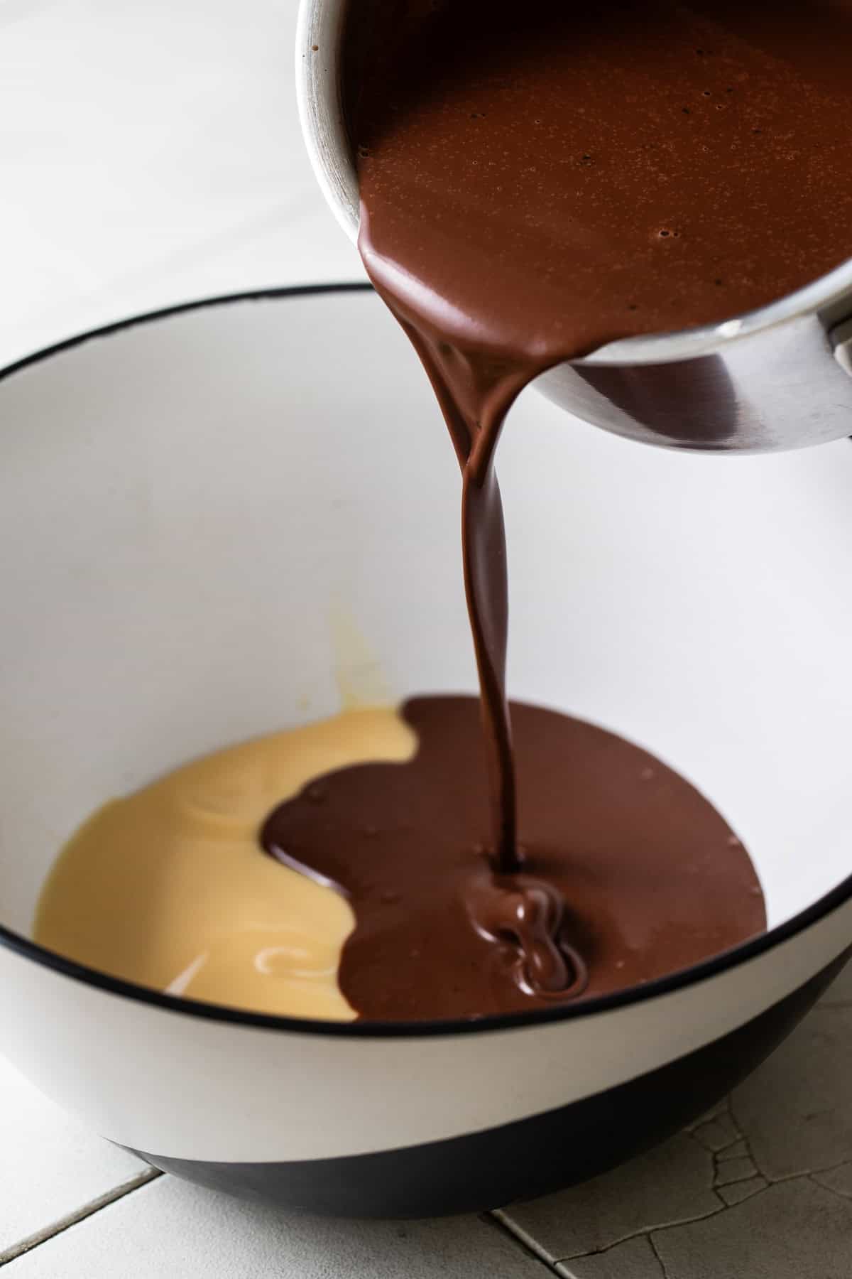Melted chocolate being poured into a bowl with sweetened condensed milk.
