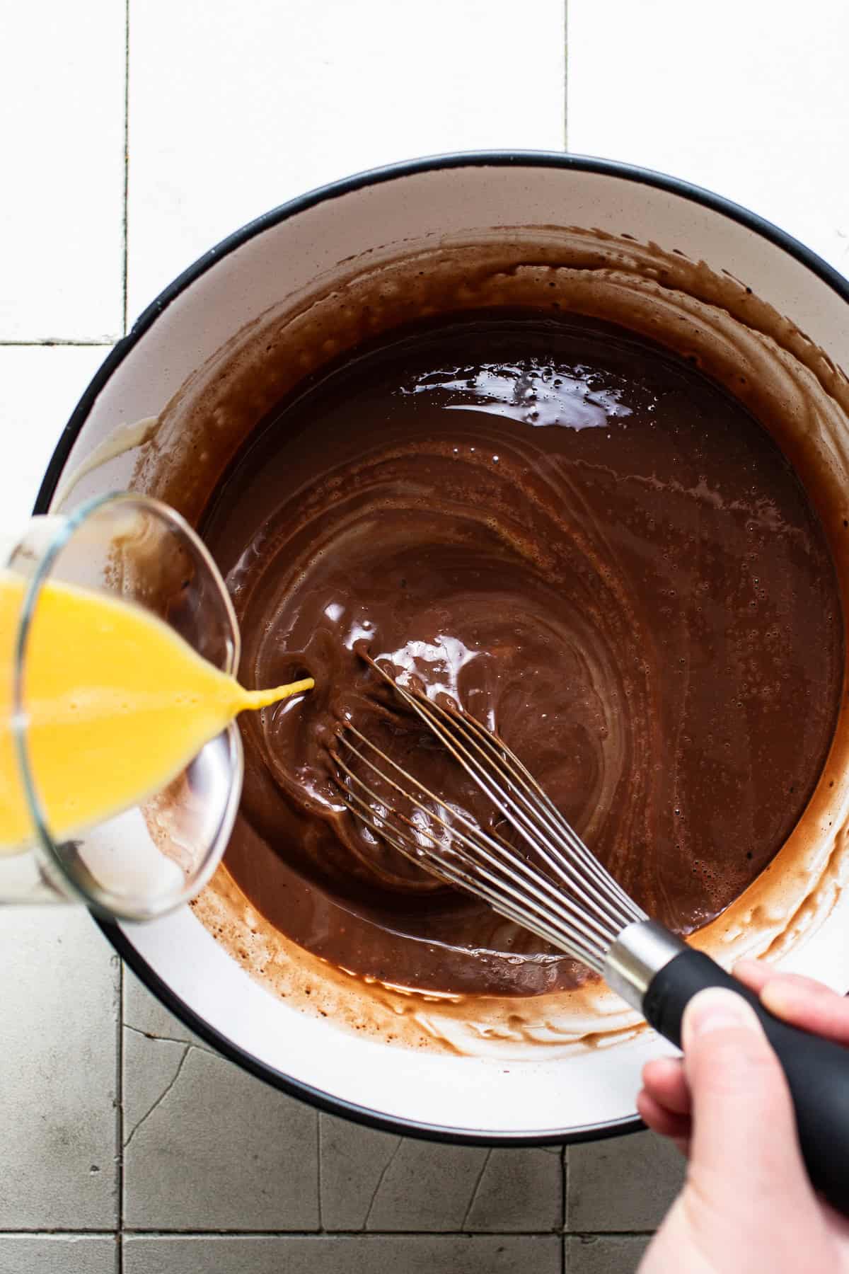 Whisked eggs being mixed into a bowl of flan mixture.
