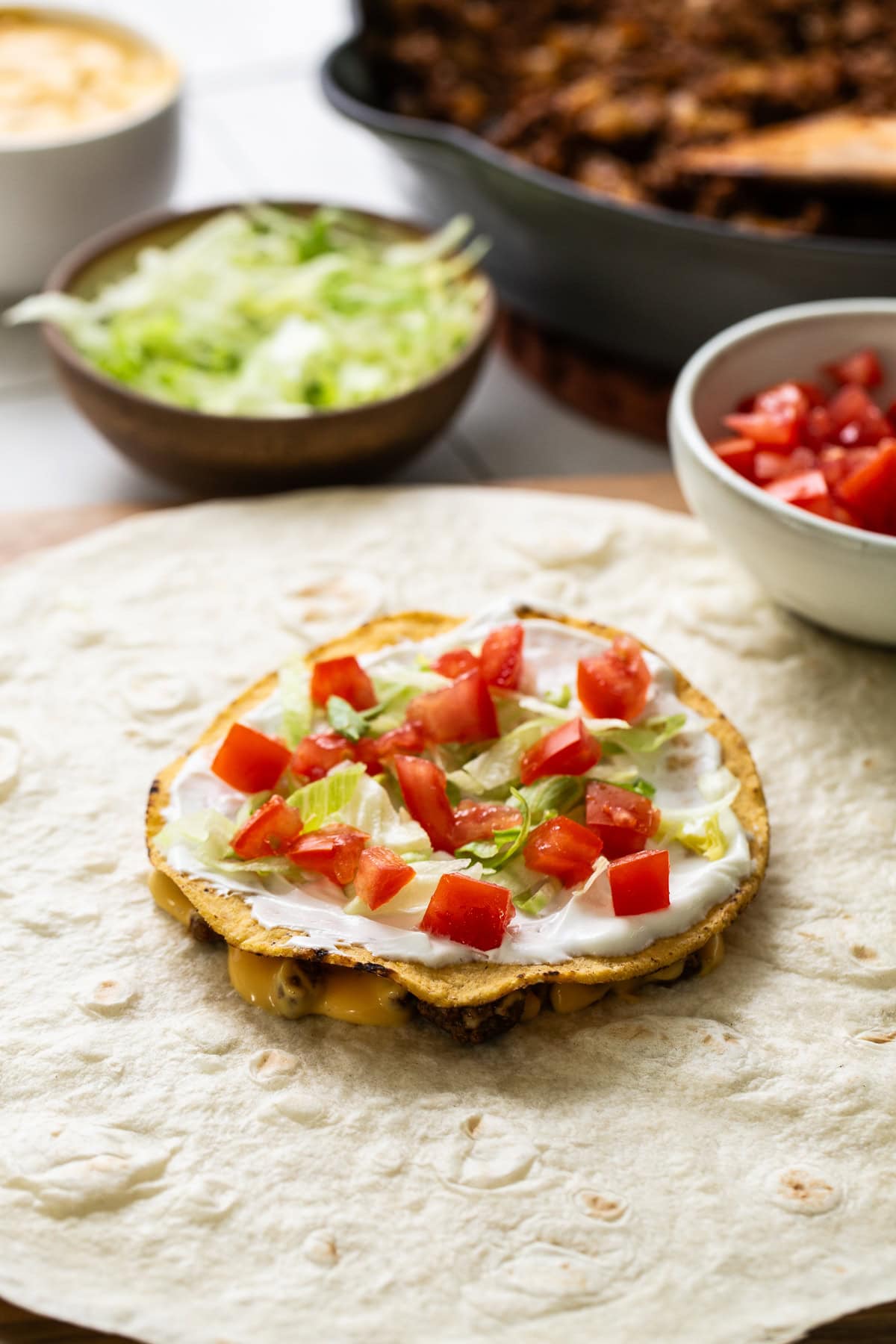 Ground beef, nacho cheese, a tostada shell, shredded lettuce, and diced tomatoes on a large flour tortilla.