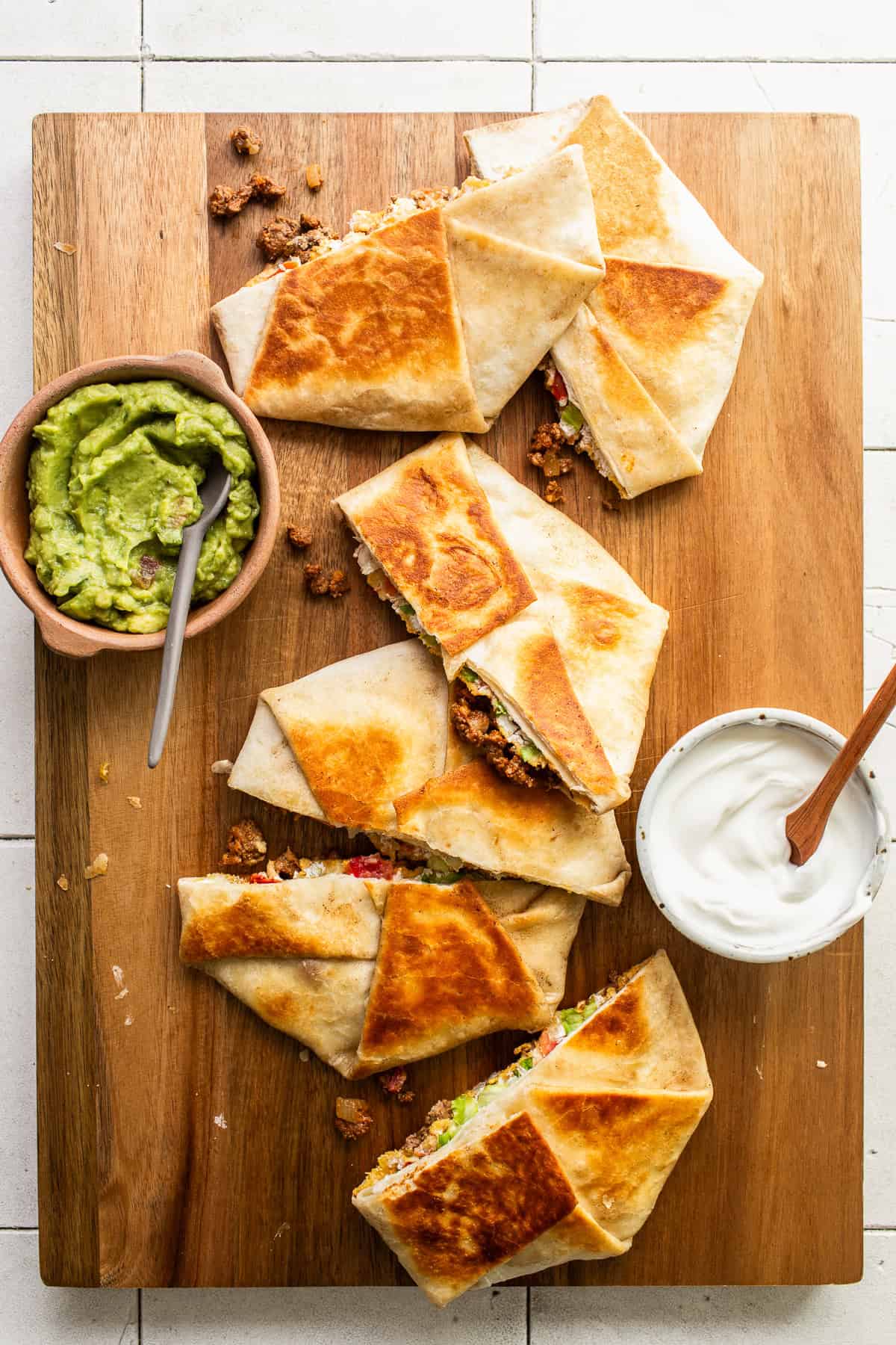 Crunchwrap supremes sliced in half and served with guacamole and sour cream.