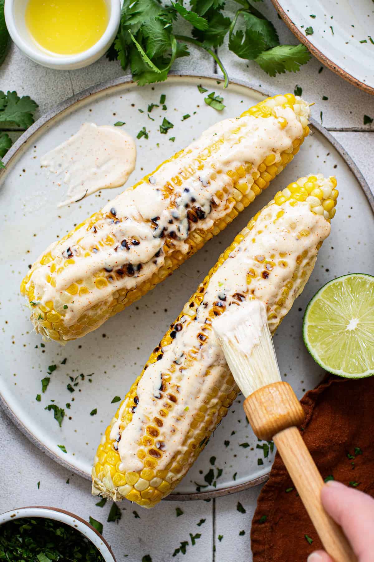 Grilled corn being brushed with mayo sauce for elotes, aka mexican street corn.