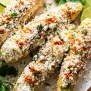Elotes on a plate with cotija cheese, mayonnaise, cilantro, and cayenne or chili powder.