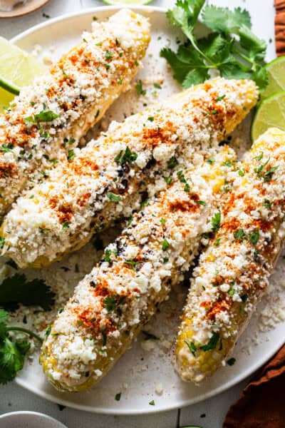 Elotes on a plate with cotija cheese, mayonnaise, cilantro, and cayenne or chili powder.