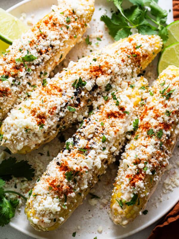 Elotes on a plate with cotija cheese, mayonnaise, cilantro, and cayenne or chili powder.