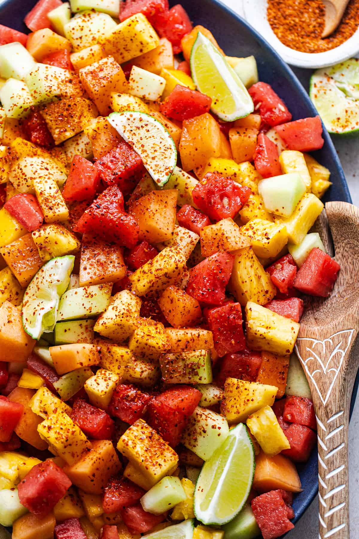 Mexican fruit salad on a serving platter sprinkled with Tajin chili lime seasoning.