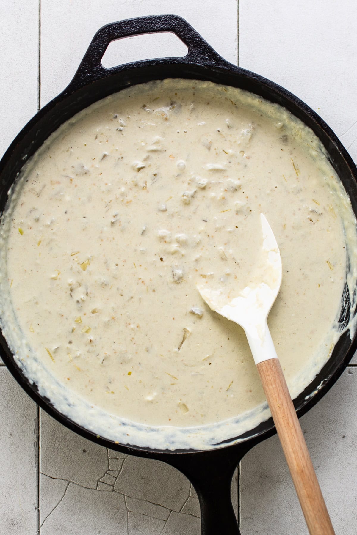 A cream cheese sauce being stirred in a skillet.
