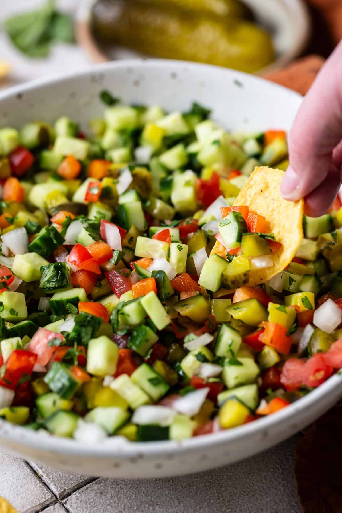 A tortilla chip being dunked into a bowl of pickle de gallo.
