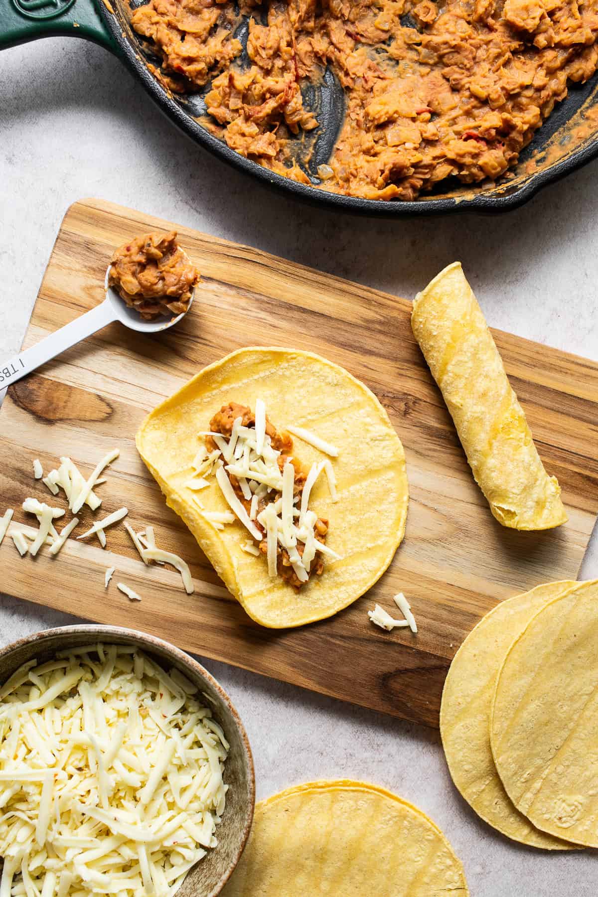 A bean and cheese taquitos being filled on a table.