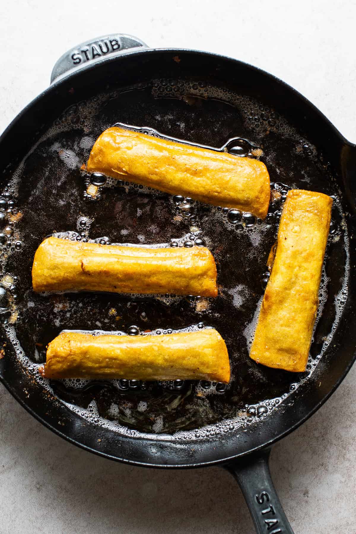 Bean and cheese taquitos frying in a skillet.