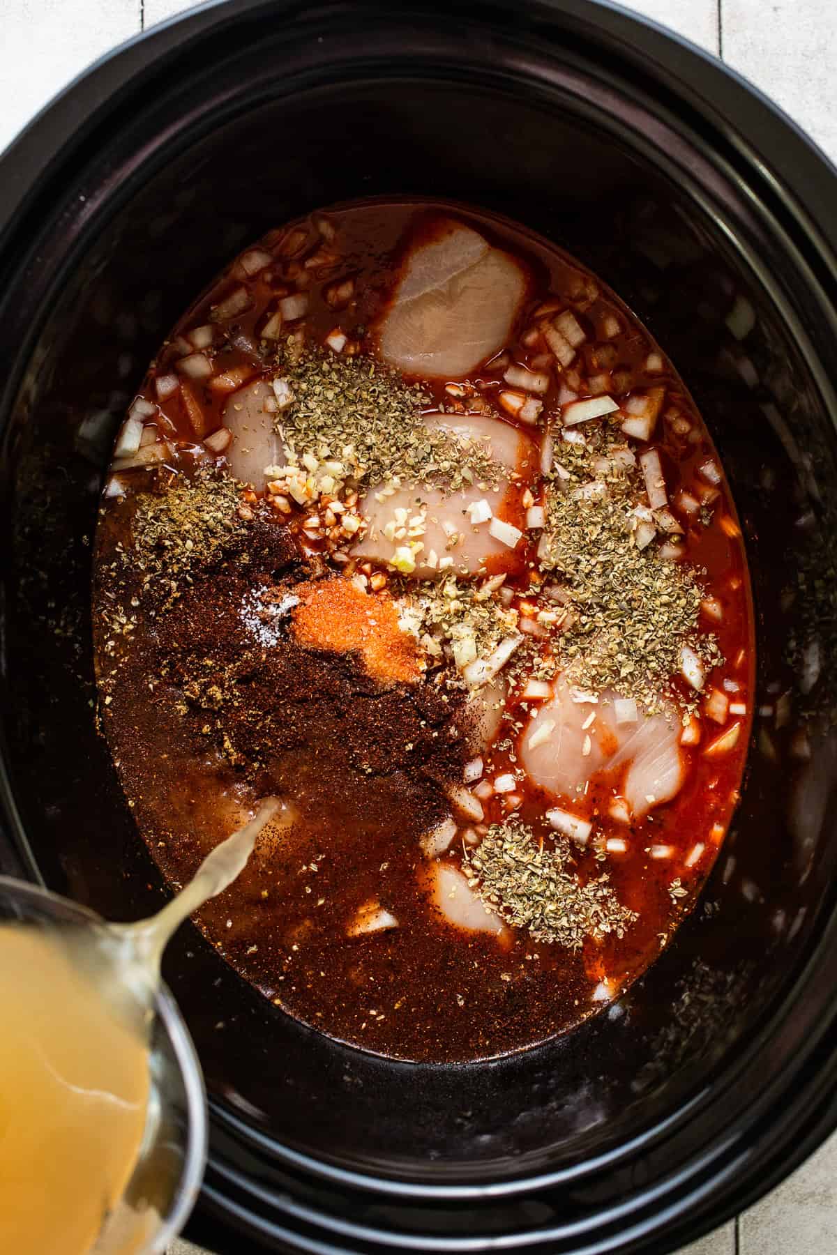 Broth being poured into a slow cooker pot to make chicken pozole.